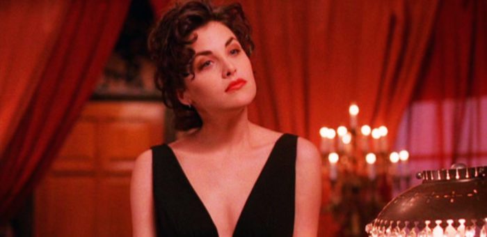 Audrey Horne (Sherilyn Finn) standing in a room with a red curtain wearing a black dress