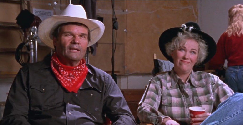 A man (Fred Willard) and woman (Catherine O'Hara) wearing cowboy hats sit backstage during a photoshoot. 