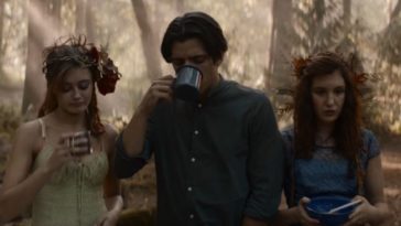 Travis takes a drink from a metal cup as Jackie and Shauna stand to each side of him in the woods in 1996 in Yellowjackets "Doomcoming"