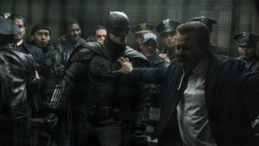 A suited police officer holds back Batman from a fight.