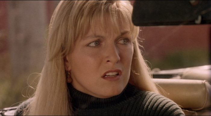 Laura Palmer, a young woman with long blonde hair, sits in the passenger seat of a car and looks to her left; her face is agitated and afraid. 