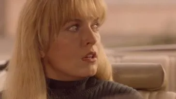 A close-up image of a young woman with long blonde hair in the passenger seat of a car. Her facial expression is one of shock.