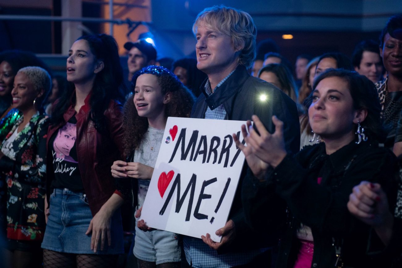 A man holds up a sign that reads "Marry Me" at a concert.