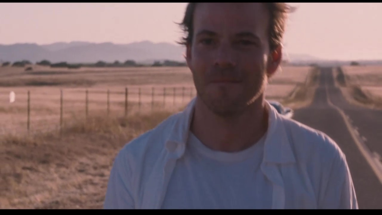 Image from Somewhere: Johnny walks away from his car in the desert and smiles.