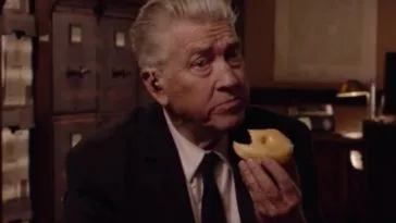 David Lynch as Gordon Cole, eating a donut and sitting in front of a vintage filing cabinet