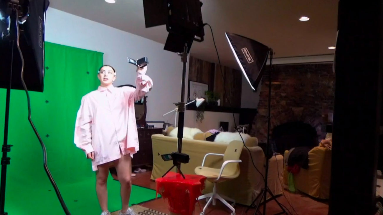 From Alone Together. Charli XCX holds a camera in front of a green screen.