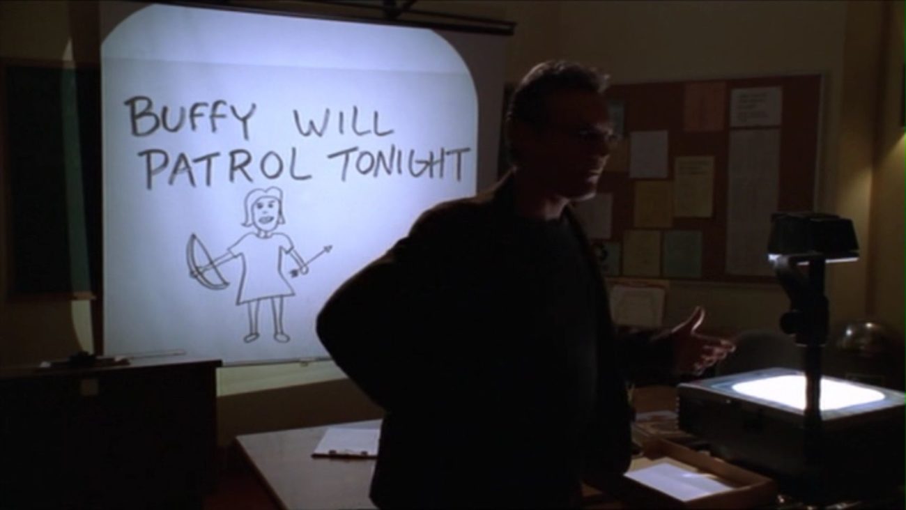 Giles using the projector to explain the situation to the group - the slide says "Buffy will patrol tonight" with a crudely-done drawing