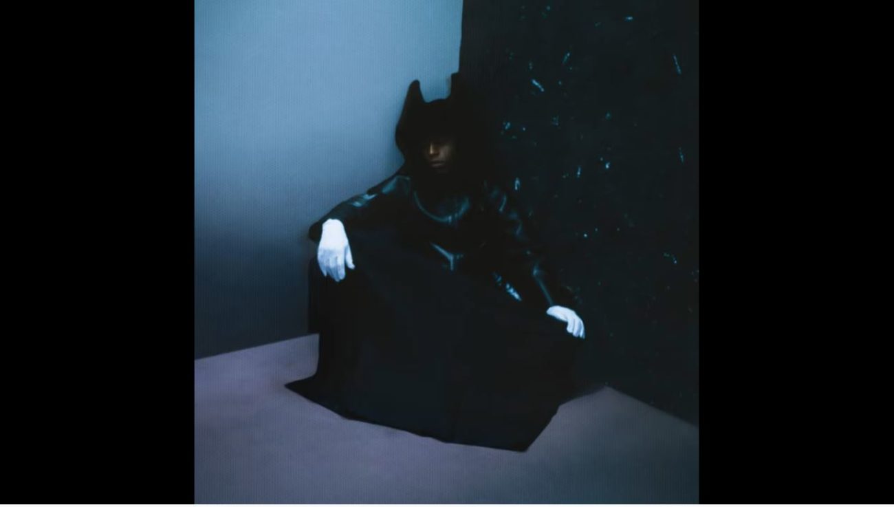 A figure in a black robe sits in the corner, wearing white gloves, on the cover of Bakar's Nobody's Home