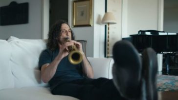 Kenny G reclines on a sofa, playing soprano sax