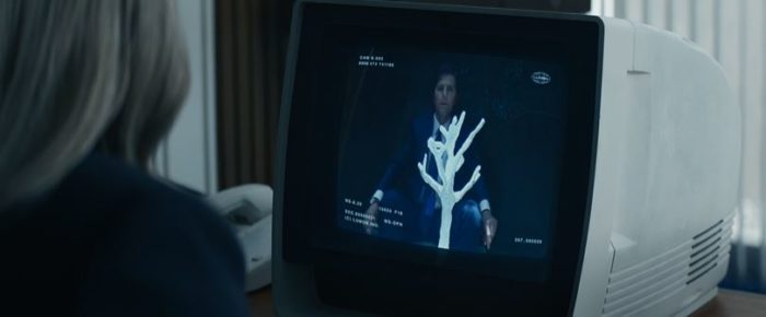 Mark on a computer screen, with a white clay tree in front of him. Harmony, from behind, is looking at the screen