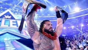 Roman Reigns holds up his two title belts