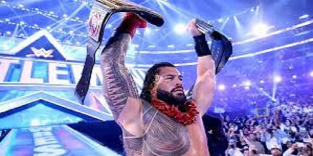Roman Reigns holds up his two title belts