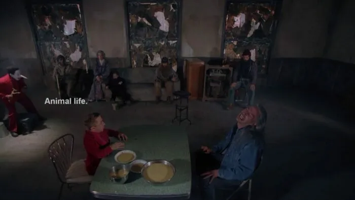 The Arm and Bob sitting at the formica table, surrounded by the Jumping Man, the Woodsmen, Mrs. Tremond and her grandson, and the Electrician.