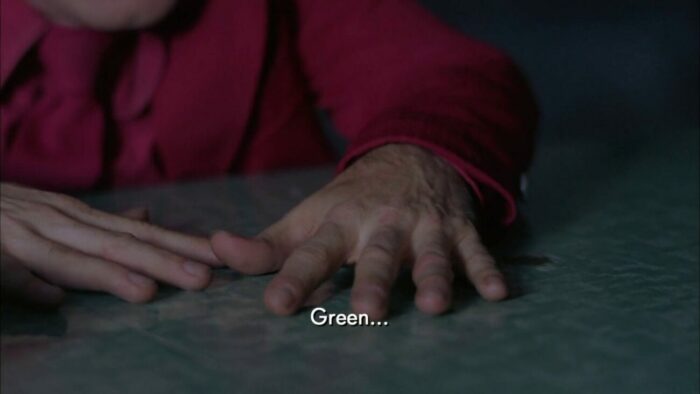 The Arm moves his hands over the green formica table.