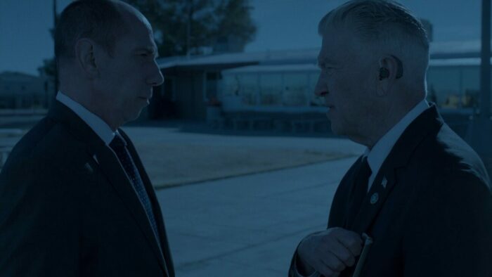 Within a blue-saturated frame, Albert and Gordon converse outside prison.