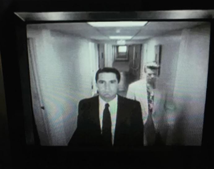 Dale looking upward on a CCTV screen as Jeffries walks by