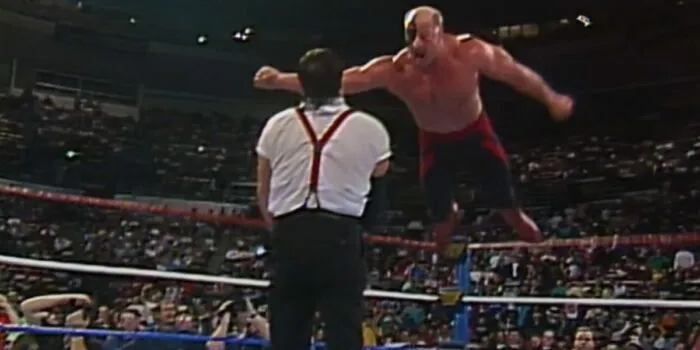 A mid-air Hawk is about to hit I.R.S. with a top rope clothesline.