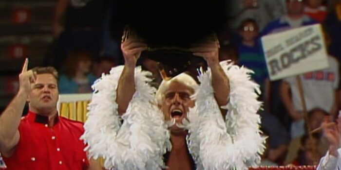 Ric Flair, in his feather boa gown, holds aloft the "world title" but it is covered by a black blur.