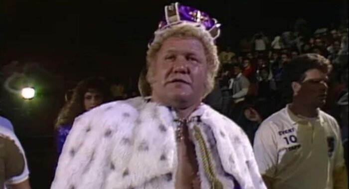 Harley Race, with fur-lined cape and purple crown, walks to the ring.