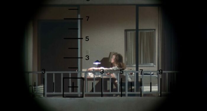 A woman being watched through a telescope while she is in her own apartment