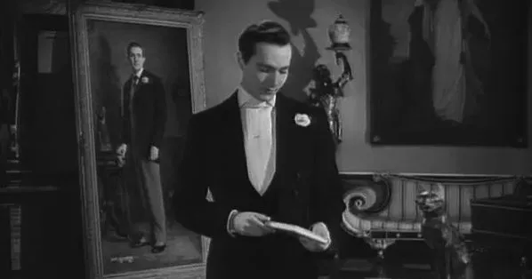 Dorian Gray stands with his back to his painting, which shows a portrait of him looking onwards