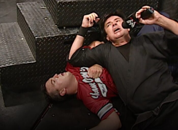 Eric Bischoff lies on top of a downed Shane McMahon at ringside