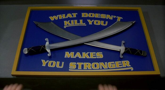 A sign with two cutlasses that reads "WHAT DOESN'T KILL YOU MAKES YOU STRONGER" in the gym in Final Destination 3 (2006)