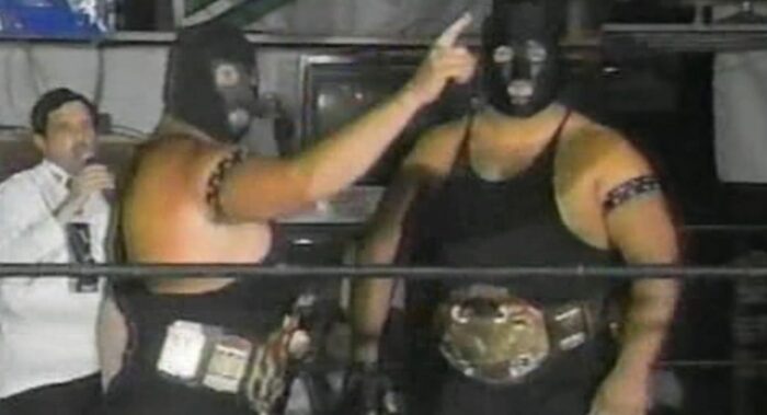 The Executioners taunt in the ring, donning black singlets and masks.