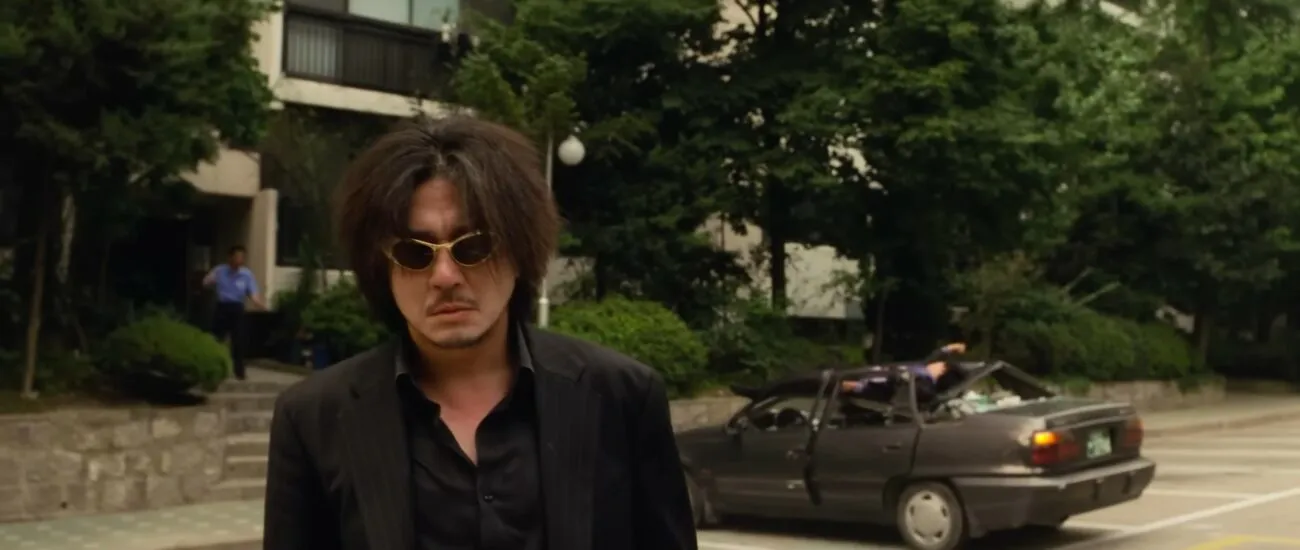 Dae-Su wearing sunglasses and walking away in the daylight