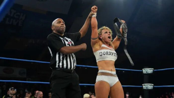 Jordynne Grace holds up her TNA Knockouts title belt as a ref holds her arm up in victory