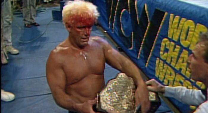 Ref Bill Alfonso hands a bloody Ric Flair the Big Gold Belt.