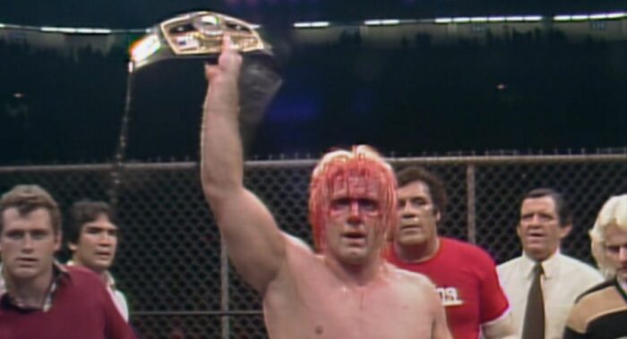 A bloody Ric Flair holds up the Ten Pounds of Gold in the cage at Starrcade '83