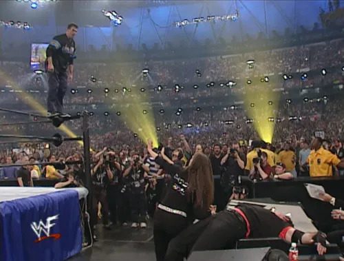 Shane McMahon is blocked from leaping at Vince McMahon, prone on a table, by Stephanie McMahon at WrestleMania X7