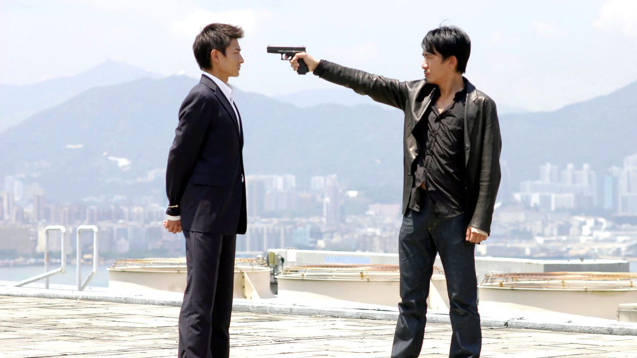 The two main characters from Infernal Affairs stand on a rooftop, one with a gun pointed to the others head, in this compelling Asian crime drama.