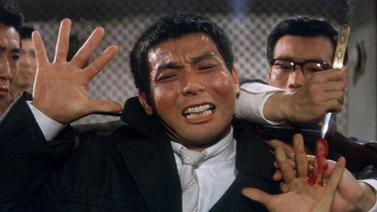 The main character from Youth of the Beast is pinned against a glass partition as the main villain pushes a blade into his finger, in the first ever true Asian crime drama.
