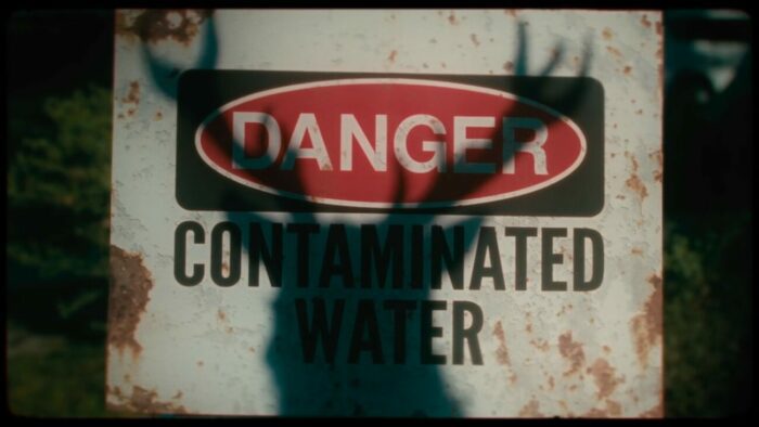 A deer's shadow is seen over a sign that says "Contaminated Water" in A Most Atrocious Thing