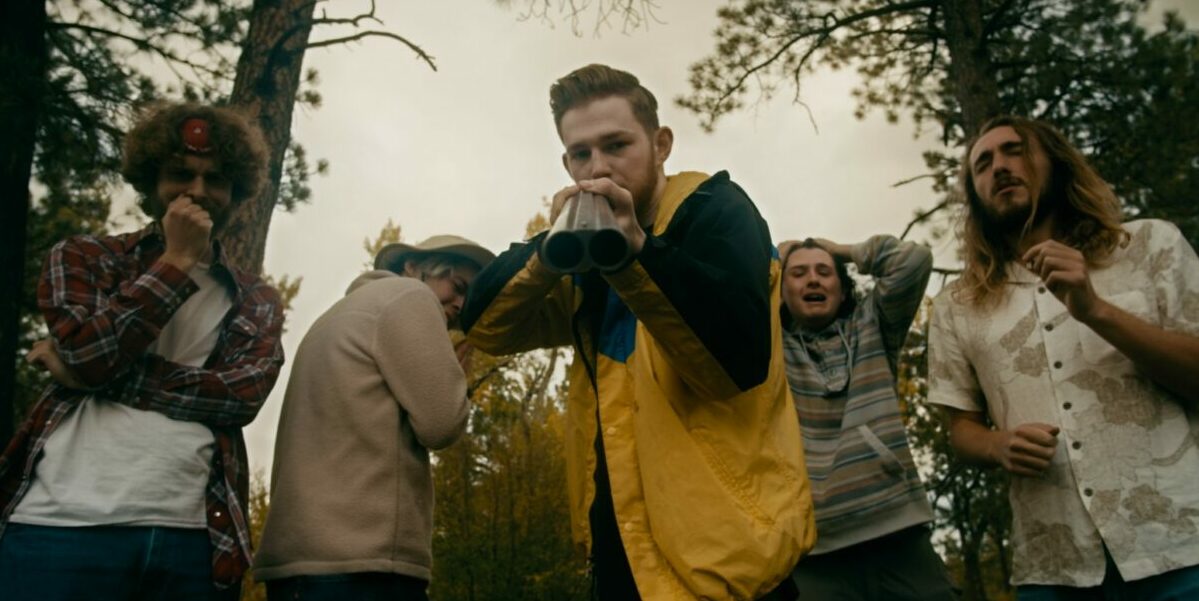 A young man holds a shotgun directly into the camera while surrounded by his squeemish group of friends in A Most Atrocious Thing