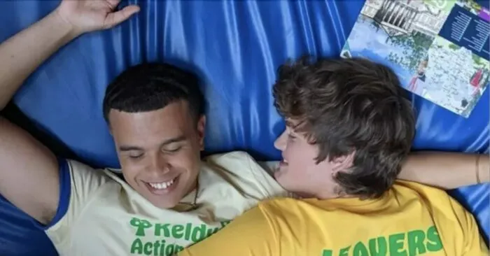 Two men smiling laying on top of one another in bed