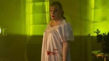 Nina is seen in the yellow light while wearing a bloody nightgown