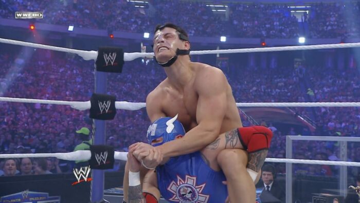 Cody Rhodes, in his protective face mask, camel clutches Rey Mysterio at WrestleMania XXVII