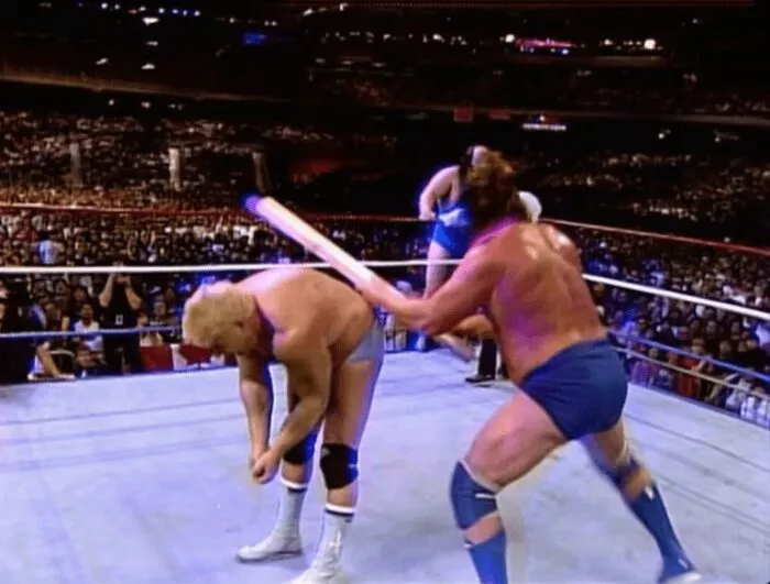 Hacksaw Jim Duggan hits Dino Bravo across the back with his 2x4