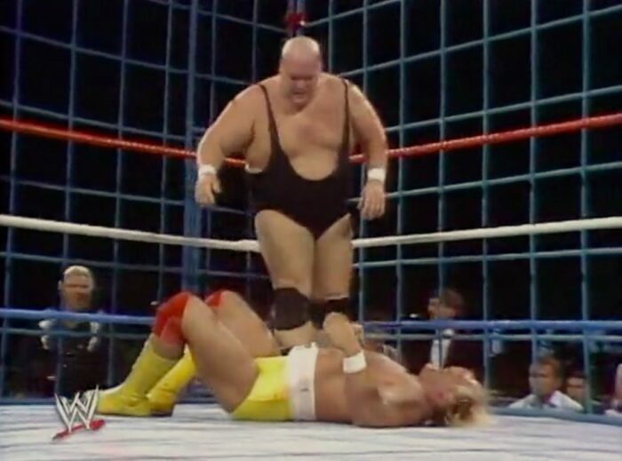 King Kong Bundy looks down at a prone Hulk Hogan in the steel cage at WrestleMania II