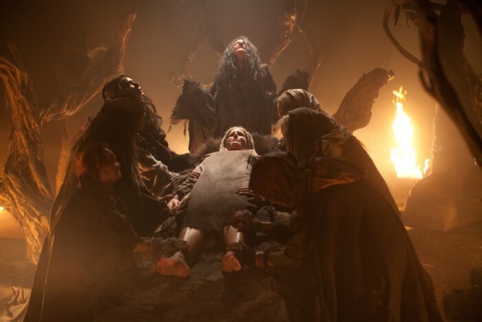 A woman lies on a table in a cave surrounded by creatures and fire in The Lords of Salem