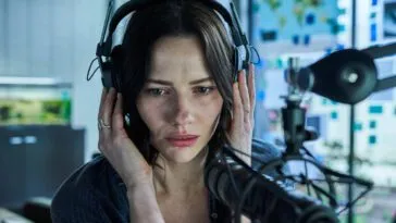 A woman sits in front of a microphone, cupping her headphones
