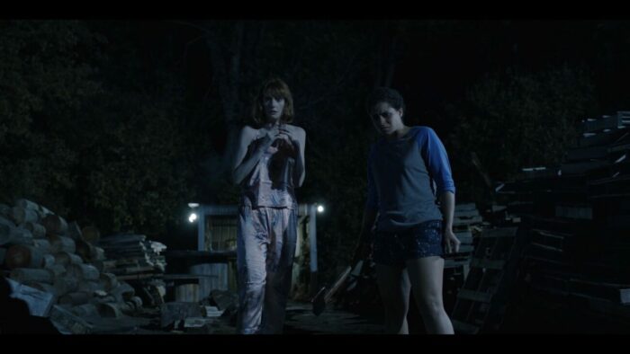 One woman in silk pajamas cowers in fear next to another woman holding an ax in Sins of the Father
