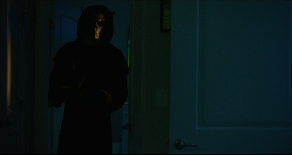 A person in a hoodie and shiny mask enters a room