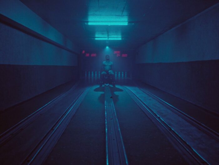 A low, blue light fills the narrow lanes of a bowling alley in The Power of the Strike