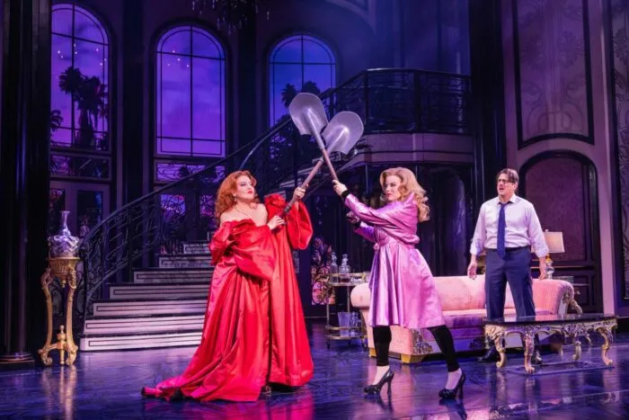 Helen Sharp (Jennifer Simard) and Madeline Ashton (Megan Hilty) spar with shovels as Ernest Menville (Christopher Sieber) watches. (Photo: Matthew Murphy & Evan Zimmerman)