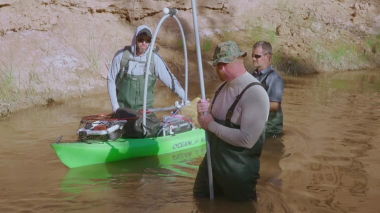 Kaleb, Thomas, and Dragon trek through the river with a kayak