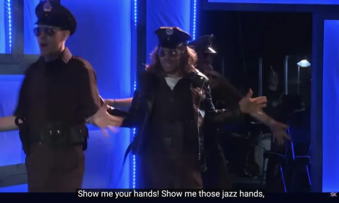 Officer Sam Sweetly (Jeff Blim), dancing with other cops, sings, "Show me your hands! Show me those jazz hands," in the musical, "The Guy Who Didn't Like Musicals."